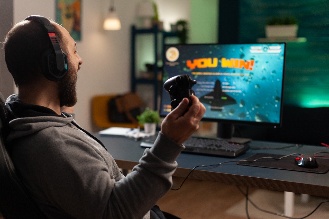 A man winning a video game, wearing headphones and holding controller game on a PC